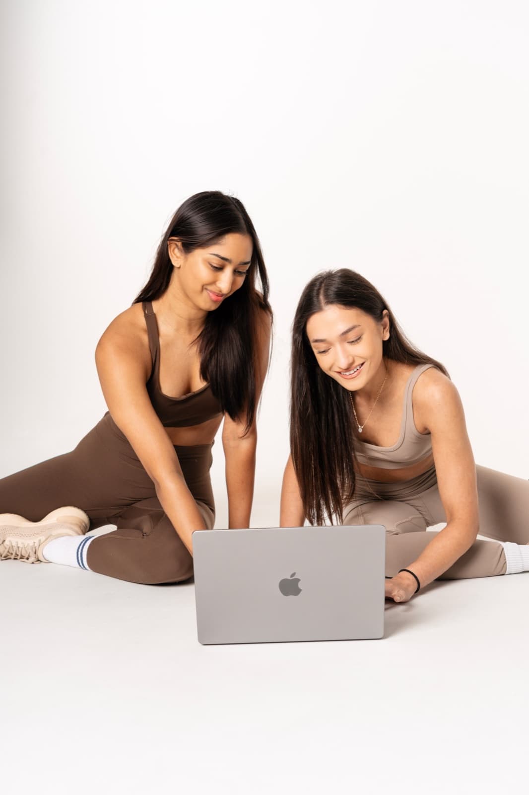 Two women laughing over a laptop in a bright studio