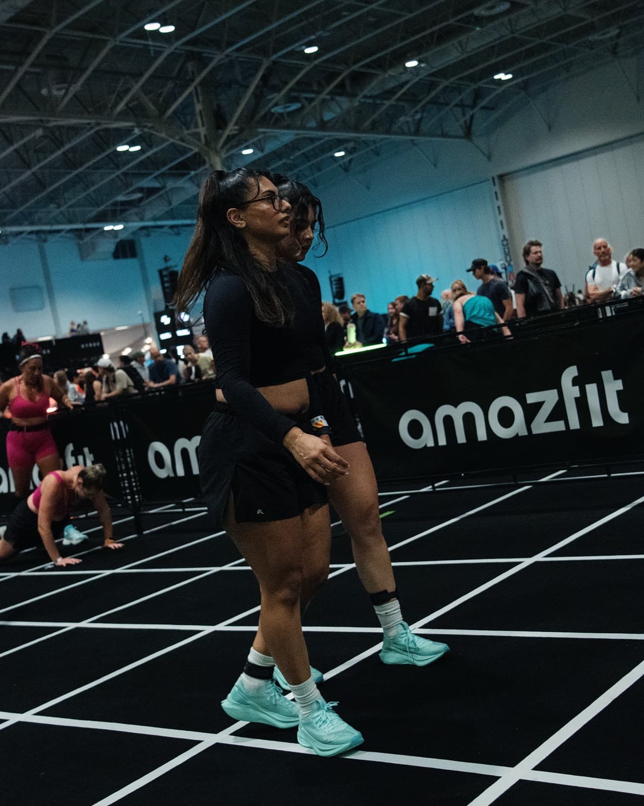 Two athletes in matching black sets walking the race floor past the Amazfit barriers