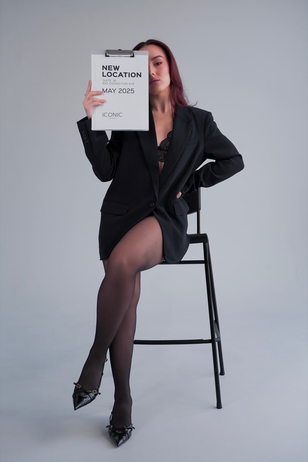 Full-length shot of the model on a bar stool holding the New Location clipboard